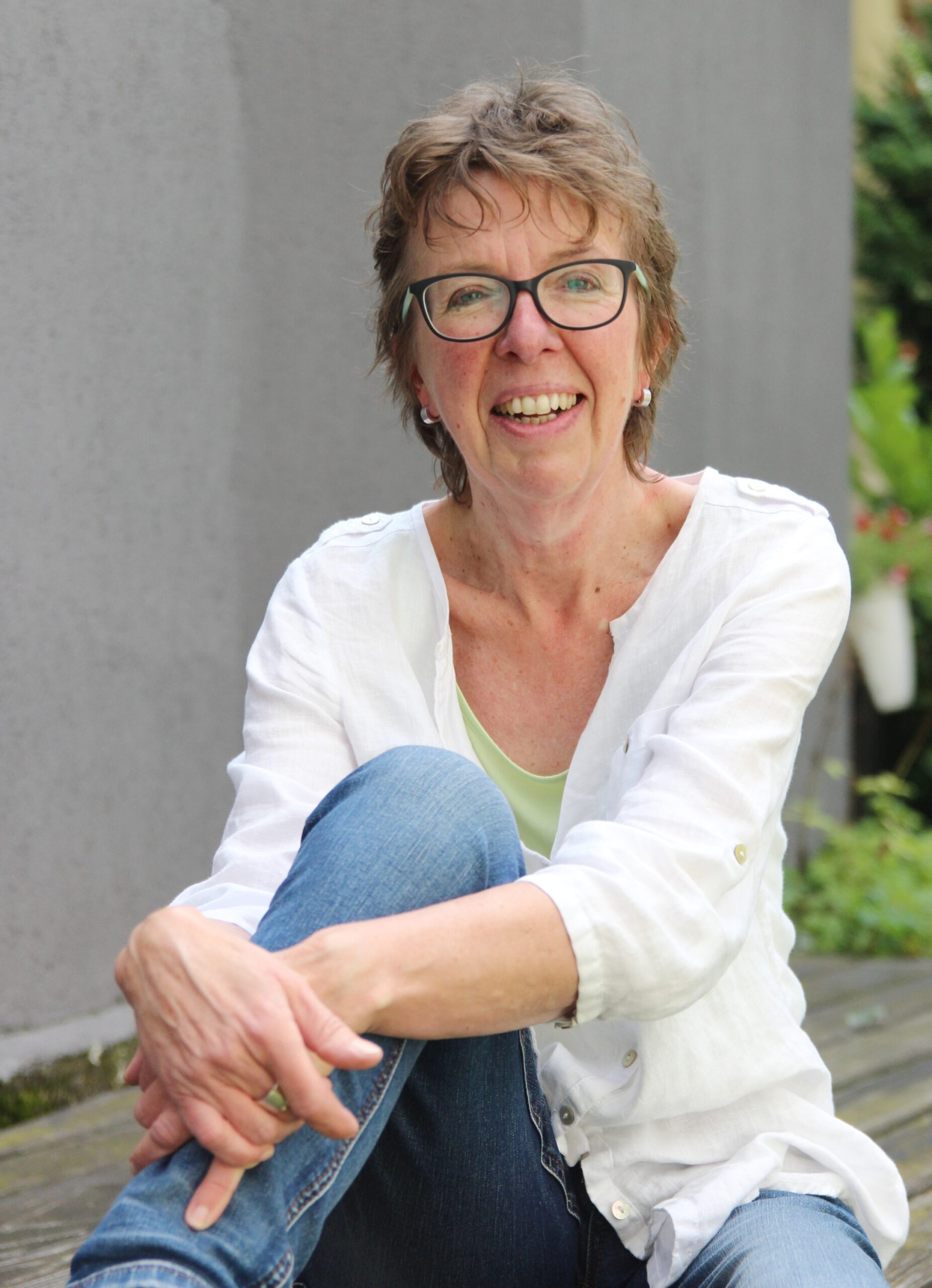 Eine Frau sitzt mit einem angezogenen Knie auf einer Sitzfläche im Freien.